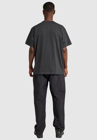 Mörkgrå t-shirt med kort ärm i bomull, tillsammans med lösa svarta byxor. Bakifrån visas en avslappnad passform och en enkel design.