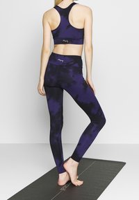 Fioletowy zestaw sportowy składający się z biustonosza i legginsów w stylu tie-dye, wykonany z elastycznego materiału, z wysokim pasem i gładką fakturą, widok z tyłu.