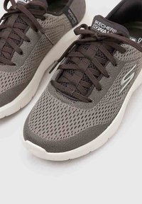 Buty sportowe Skechers z szarym siateczkowym wierzchem, ciemnymi sznurowadłami i białą gumową podeszwą, z teksturowanym wzorem i logo na języku.