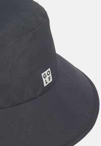 Mørkeblå bøttehat lavet af letvægtsstof, med en bred skygge og et lille hvidt firkantet logo med teksten "GOLF." Glat tekstur.