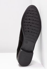 Schwarzer Wildlederschuh mit einer strukturierten Gummisohle, die über ein dezentes eingeprägtes Logo und ein gemustertes Profil für besseren Halt verfügt.