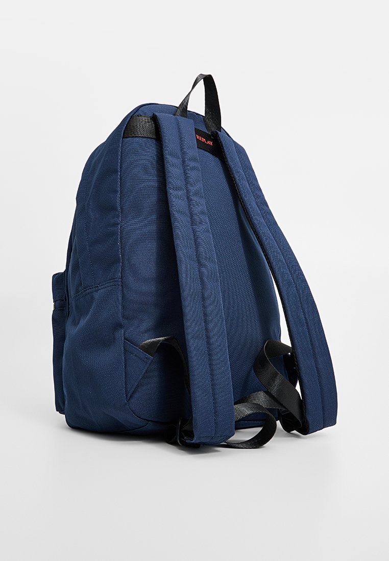 Zaino in tessuto blu navy con spallacci imbottiti, due tasche laterali e un piccolo logo rosso nella parte superiore. Tessuto liscio con cuciture rinforzate.