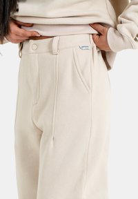 Beige sweatpants van zachte stof, met een aansluitende taille, voorzakken en een klein merkje op de tailleband.