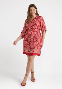 Red patterned dress with short sleeves, cinched waist, and a hemline above the knee. Decorative white floral motifs and trim detail.