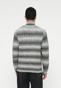 Szary sweter w paski z wysokim kołnierzem, wykonany z grubej, teksturowanej tkaniny. Posiada ściągacze na dole oraz przy mankietach, a także luźną sylwetkę.