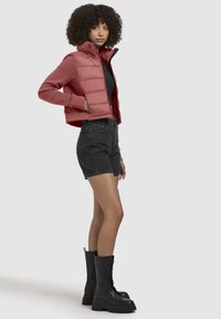 Korte roze pufferjas over een zwart topje, gecombineerd met zwarte denim shorts en zwarte veterboots tot de enkel. Zachte en textuurrijke materialen.