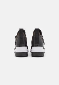 Zwart-grijze sneakers met een gebreide textuur, een witte tussenzool en glanzende zwarte accenten. Voorzien van een trekkoord en logo-details op de hiel.