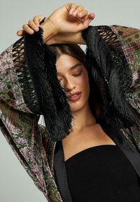 Haine exterioare lungi, în stil kimono, cu un model verde și burgund, marginile cu franjuri negri și interior din satin negru. Material texturat, croială lejeră.