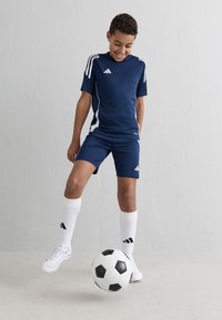 Jūras spēka sporta apģērbs ar baltām akcentēm, kurā ir īsām piedurknēm t-krekls un šorti. Baltas futbola zeķes un melnbalts futbola bumbas komplekts.