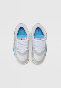 Baskets de sport grises et blanches avec des accents bleus, présentant une texture lisse, un bout rond, des lacets blancs et un logo rouge sur la languette.