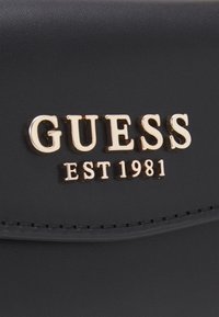 Portafoglio in ecopelle nera con logo "GUESS" in oro metallizzato e dettaglio "EST 1981" impressi. Texture liscia con dettagli cuciti.