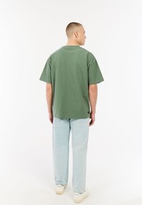 Groene katoenen T-shirt met een losse fit en korte mouwen, gecombineerd met lichtblauwe spijkerbroek en witte sneakers.