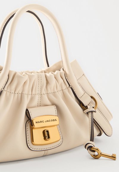 Sac à main en cuir beige Marc Jacobs avec haut froncé, fermoir doré, doubles poignées et clé décorative dorée attachée à la lanière.