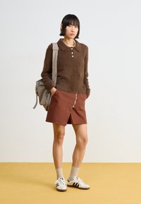 Brown fuzzy sweater with collar and button details, paired with a brown skirt featuring a front slit. Worn with white sneakers and light socks.