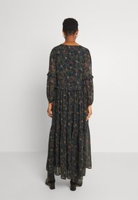 Lång svart blommig klänning med långa ärmar, volangdetaljer och ett lager på lager-skirt. Har ett flerfärgat blommönster på ett genomskinligt överdrag.