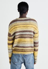 Pull en tricot avec des rayures jaunes, marron et bleues. Texture douce, coupe décontractée, et un col rond, associé à un jean bleu.