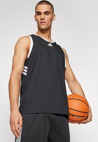 Černý sportovní tílko s bílými akcenty, které nese logo Adidas. Model drží oranžový basketbal a má na sobě odpovídající černé šortky.