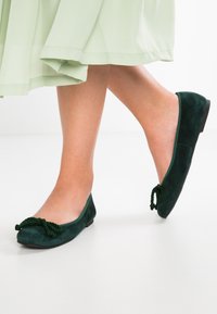 Ballerine in suede verde con finitura testurizzata, dotate di un accento decorativo annodato sulla punta e una suola bassa e piatta.