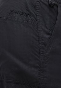 Κοντινή λήψη μαύρου εξωτερικού ενδύματος της μάρκας Houdini που δείχνει υφή υφάσματος πλέγματος και λεπτομέρειες ραφής.