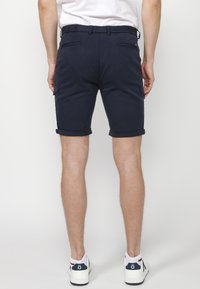Shorts bleu marine en coton avec des revers, dotés de deux poches arrière et d'une petite poche latérale, idéaux pour un style décontracté.