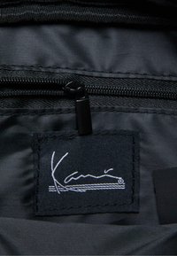 Zwart stoffen interieur met een ritsvak, voorzien van een label met de witte cursieve "Kani"-logo en een berggrafiek.
