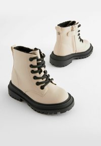 Beige leren enkelboots met zwarte veters en een gestructureerde zwarte rubberen zool. Binnenvoering van zacht zwart bont. Zijritssluiting.