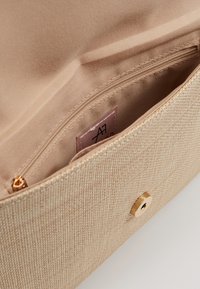 Interno di una borsa beige testurizzata con una tasca con zip, fodera liscia e chiusura a scatto con accessori in oro. Etichetta visibile vicino alla tasca.