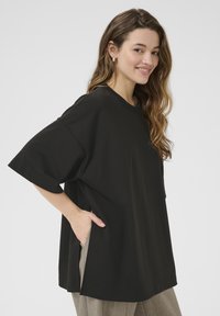 Sort oversized T-shirt med korte ærmer, rund halsudskæring, sidesplitter og en afslappet pasform. Blødt bomuldsstof giver en glat overflade.