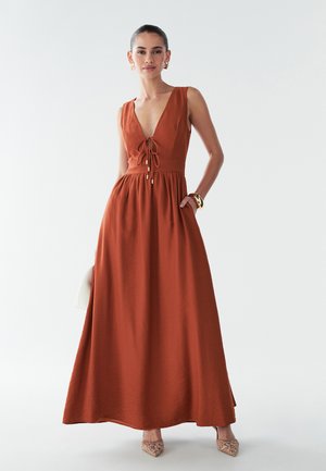 Maxi šaty v rezavé barvě, které mají hluboký výstřih do V, nastavitelné zavazování v přední části a volnou sukni. Hladká látka s mírnou strukturou a kapsami.