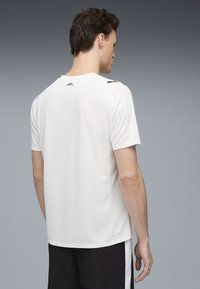 Camiseta atlética blanca de manga corta con un acabado texturizado. Presenta detalles en negro en los hombros y un logo cerca del escote.