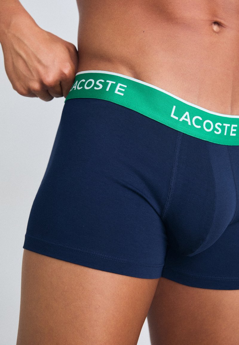 Caleçons boxers bleu marine avec une ceinture élastique verte et blanche embossée du logo "LACOSTE". Tissu doux et lisse avec une coupe ajustée.