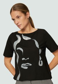 Zwarte korte mouwen T-shirt met een zilveren abstract gezicht ontwerp. Gemaakt van zachte stof met een relaxte pasvorm en een ronde halslijn.