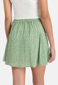 Groene bloemenrok met een geplooide tailleband en geplooid ontwerp, gemaakt van een zachte stof met een klein wit bloemenpatroon.