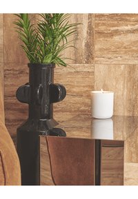 Alto vaso in ceramica nera con pianta verde accanto a una candela bianca accesa su una superficie in marmo marrone riflettente e parete in piastrelle.