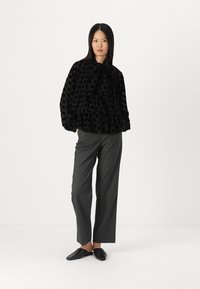 Black polka dot blouse with ruffles and a tie neck detail, paired with gray pinstriped trousers and black slip-on shoes.