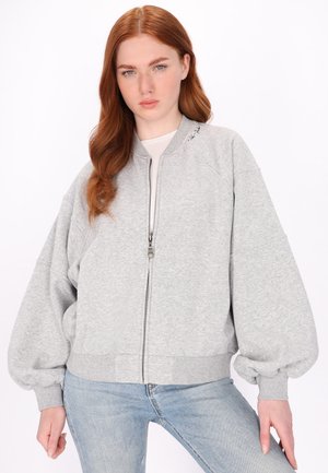 Svetle šedá bomber bunda na zip s oversized rukávy, žebrovanými manžetami a lemem, vyrobená z měkké tkaniny. Na límci je minimalistické logo.