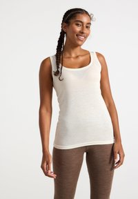 Canottiera beige chiaro con scollo a giro, realizzata in tessuto morbido e strutturato. Abbinata a leggings marroni, strutturati e con una vestibilità aderente.