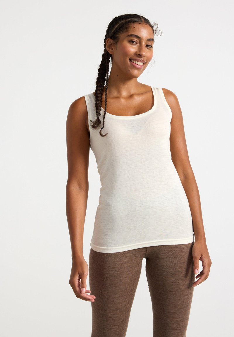 Canottiera beige chiaro con scollo a giro, realizzata in tessuto morbido e strutturato. Abbinata a leggings marroni, strutturati e con una vestibilità aderente.