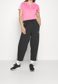Rosa Adidas t-shirt med rund hals och tre vita ränder på ärmarna, i kombination med svarta sweatpants med vita sidränder och snörning.