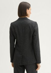 Dark grey tailored blazer made of textured fabric, featuring a classic collar, structured shoulders, and vent at the back.