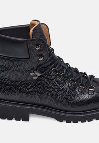 Stivale da trekking in pelle nera effetto textured con applicazioni in metallo, design con lacci e suola robusta. Presenta un rivestimento interno in contrasto di colore marrone.