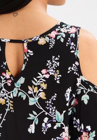 Blusa nera floreale con design a spalle scoperte, caratterizzata da vivaci motivi floreali, tessuto morbido e una piccola apertura a forma di chiave sul retro.