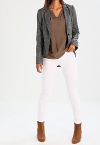 Blazer à carreaux gris sur un chemisier marron, associé à un jean skinny blanc et des bottines marron. Présente un design ajusté et une coupe slim.