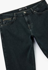 Jeans w ciemnym denimu o prostym kroju. Posiadają pięć kieszeni, kontrastowe przeszycia oraz zapięcie na guzik i zamek błyskawiczny. Rozmiar W32 L32.