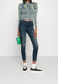 Top corto de manga larga con un patrón a rayas azul-verde, combinado con jeans skinny oscuros. Bolso verde y zapatillas negras con suelas blancas.