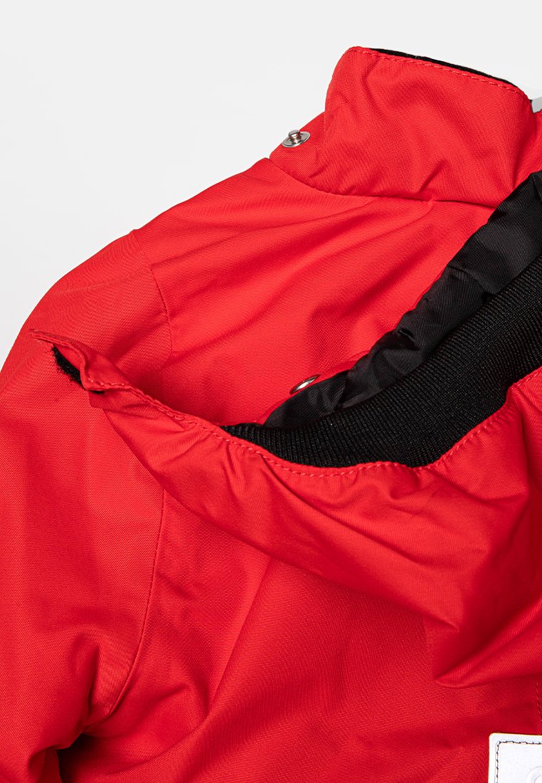 Chaqueta impermeable roja con cuello alto, que cuenta con un forro interior negro y cierre a presión en el cuello. Se puede ver una tela crujiente y texturada.