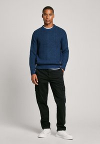 Maglione a coste navy con scollo rotondo, abbinato a pantaloni cargo neri e sneakers bianche. Focus sulla texture e sul fit sartoriale.