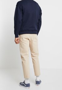 Sudadera azul marino, pantalones chinos beige, calcetines blancos y zapatillas azules. La sudadera tiene un dobladillo acanalado; los chinos son de corte recto con bolsillos traseros.