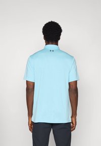 Jasnoniebieska koszulka polo z teksturowanej tkaniny, z krótkimi rękawami i czarnym logo na tylnej części kołnierzyka. Swobodny krój z tradycyjnym wzorem kołnierza.