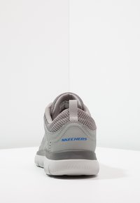 Gray Skechers sneaker with mesh upper, padded collar, and contrasting blue logo. Cushioned white sole and textured heel accent.